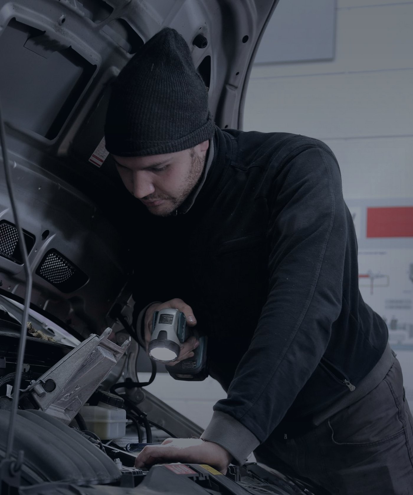 Mechanic inspecting an engine bay with a torch in a workshop