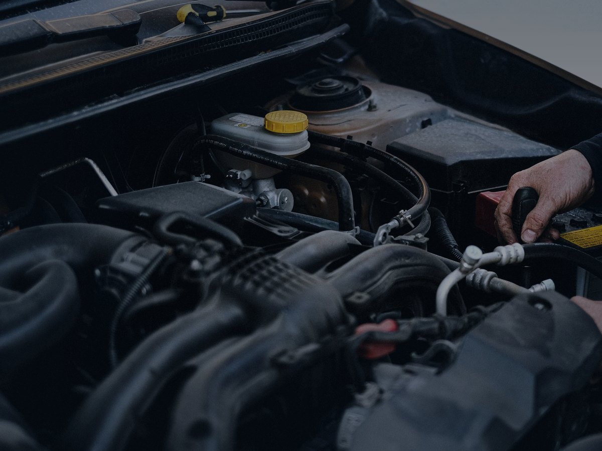 Hands working around hoses and a battery in a vehicle engine bay