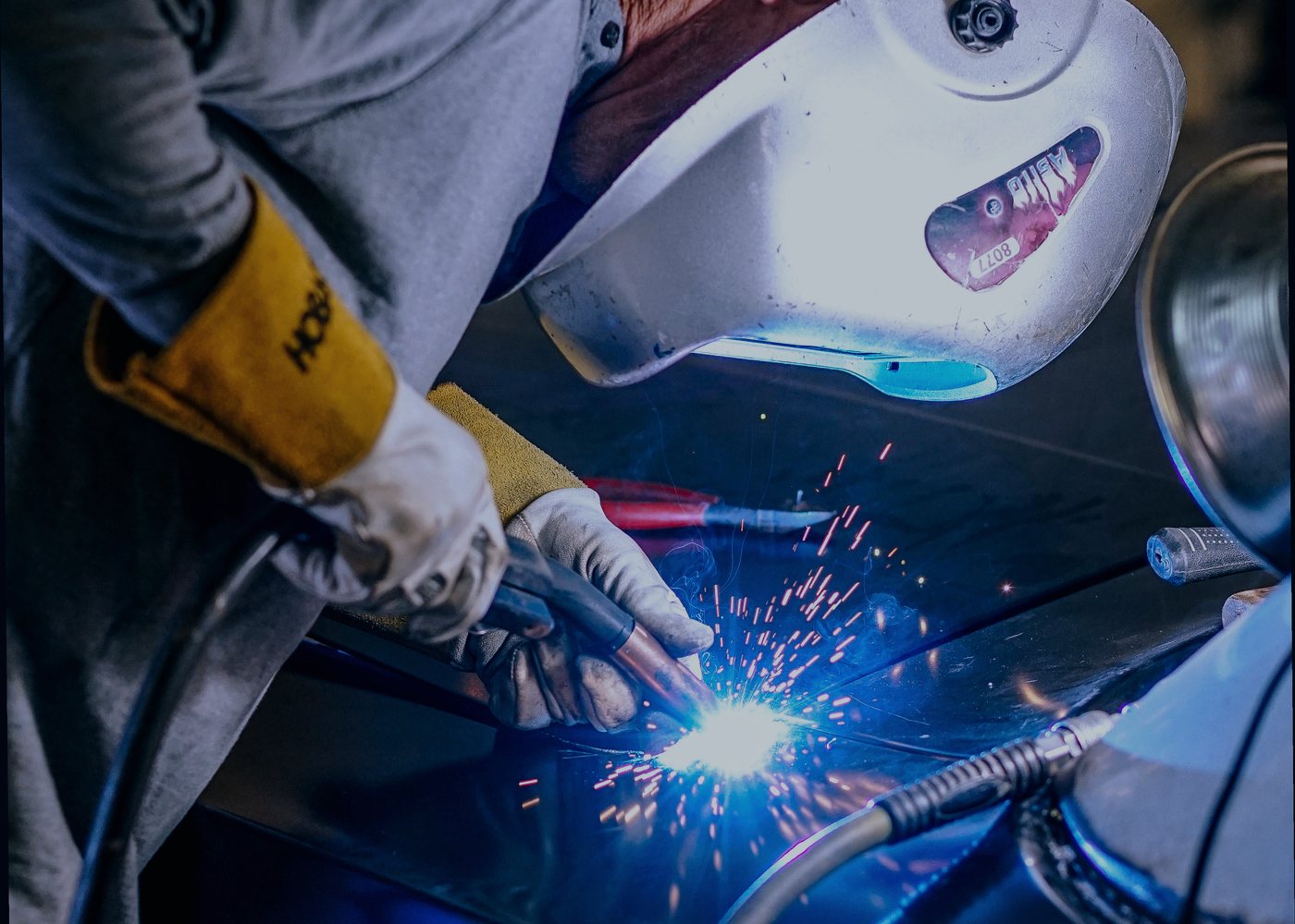 Welder in a helmet MIG welding a car body panel with sparks