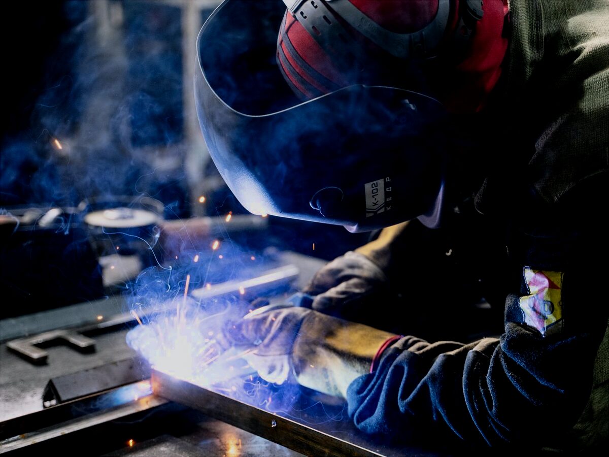 Welder in a helmet joining steel on a fabrication bench